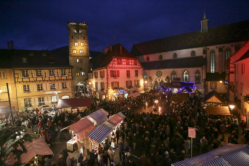 Place de village alsacien décorée pour Noël de nuit avec sapin lumineux et ambiance féerique
