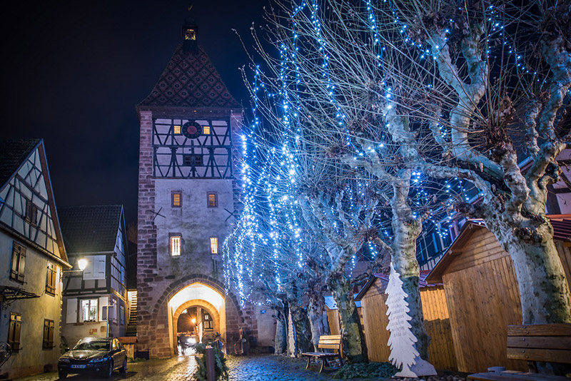 Allée nocturne d'un marché de Noël en Alsace avec stands illuminés et visiteurs